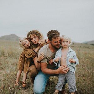 a gorgeous family of four, including two little blonde toddlers, snuggle together in a field under the sunset at a family photo session