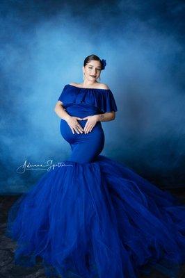 Maternity photo of mama wearing a royal blue tulle skirt standing in front of a blue backdrop