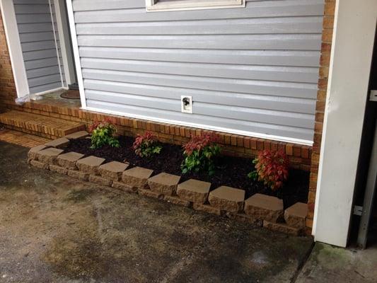 Removed plants, rocks, and timbers. Installed a small retaining wall, mulch, and colorful nandinas. 