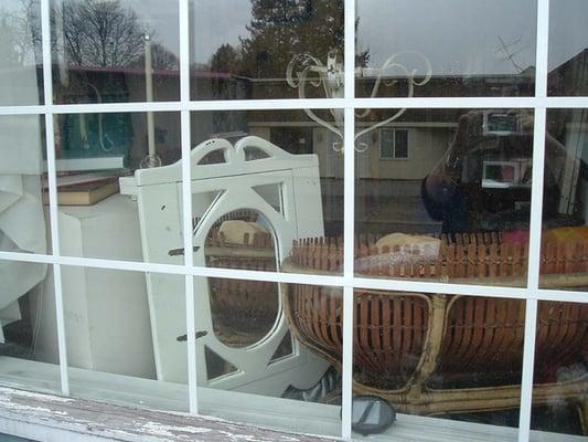 A window view of many vintage products. a bathroom mirror, a child's woven crade from the 1800's. Vintage, vintage, vintage.