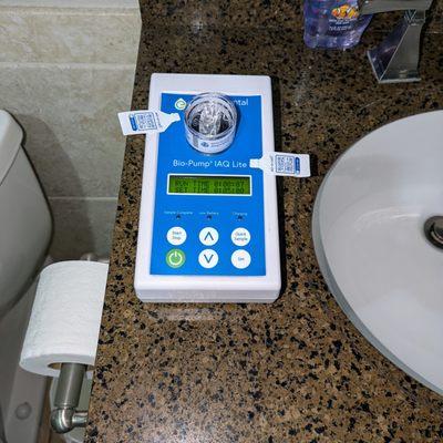 A white Bio-Pump IAQ Lite air quality testing device on a bathroom countertop with sampling cassettes attached.