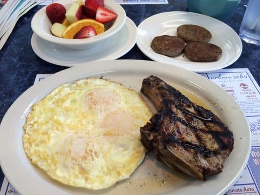 Pork chop and eggs, side of sausage patties and a side of fruit.