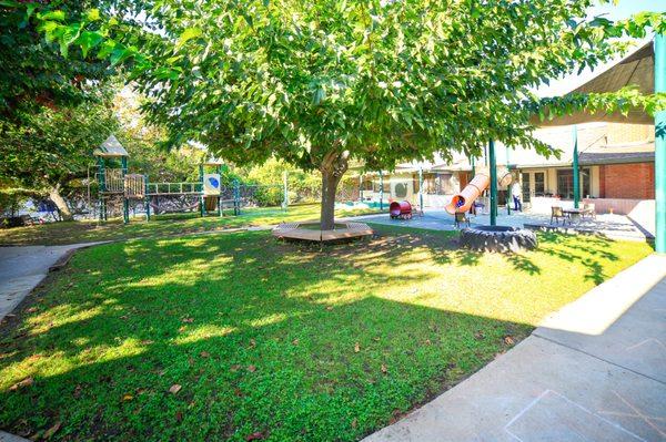 Play yard: two play structures, a climbing wall, sliding pole, slides, monkey bars, tricycle track, grassy area, and planters for gardening.