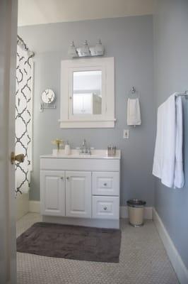 Updated bathroom with grey paint, curved shower rod, inexpensive vanity, towel hardware, light fixture, and wall mount mirror.