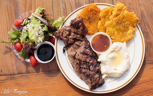 Rib-eye steak meal with plantains, mashed potatoes and side salad. ©@julieimagery