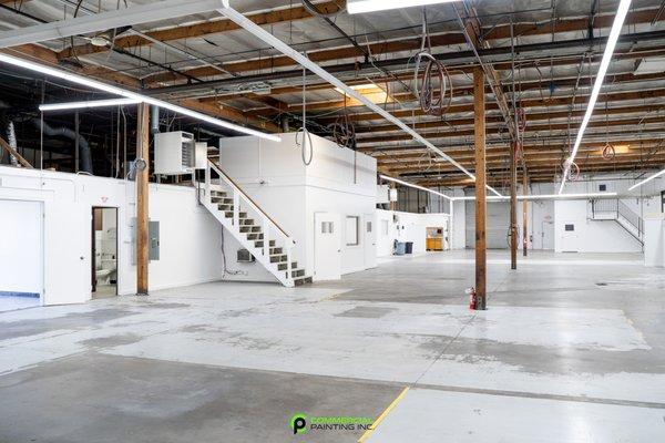 Freshly painted interior walls of a warehouse, main space with two sets of stairs and office space.