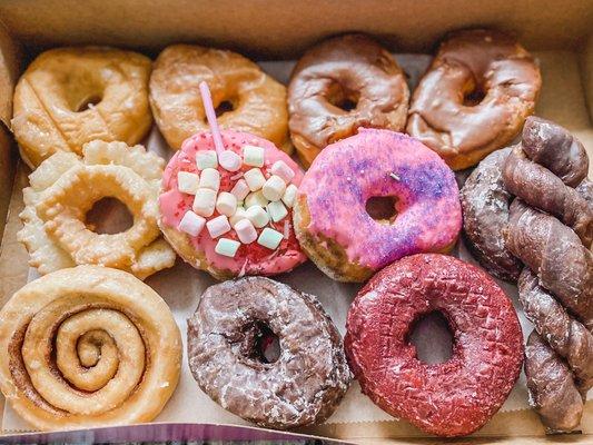 A dozen variety including glazed, chocolate iced, cruller, strawberry, cinnamon bun, red velvet, chocolate twist, and chocolate cake donut.