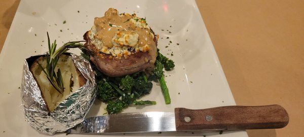 Bacon wrapped filet mignon on top of broccoli rob with a baked potato.