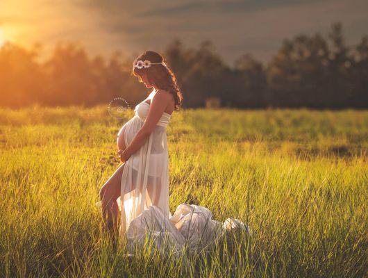 Maternity photo of mom in a grass field wearing a cream colored flow dress at photoshoot with Las Vegas, NV Maternity Photographer