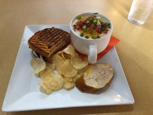 A cup of loaded baked potato soup. Along with half of a grilled portobello mushroom sandwich .