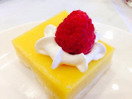 Lemon bar topped with whipped cream and a fresh raspberry