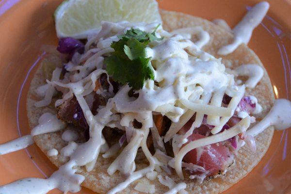 Baja Beach Fish Taco with grilled sushi-grade ahi tuna, citrus slaw, lime-cilantro crema, jack cheese served on a gluten free corn tortilla