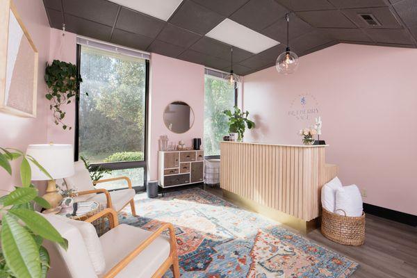 Enter the Blueberry Sage Healing Studio lobby with comforting pink walls, light wood, touches of texture, and vibrant green plants.