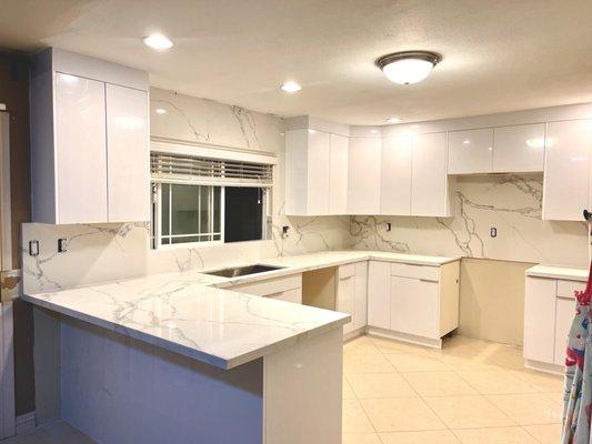 Glossy White European Style Cabinets and Pegasus Quartz Full Backsplash with Wrapped window wall.