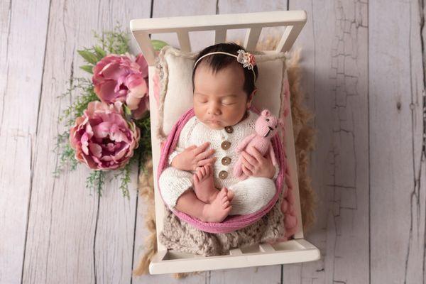 newborn girl on bed holding pink teddy bear