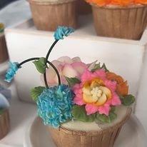 A single cupcake topped with vibrant blue and pink buttercream flowers, resembling a miniature bouquet.