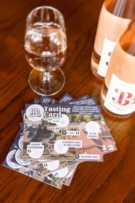 Glass of Three Brothers wine next to the wine bottle and a pile of tasting cards