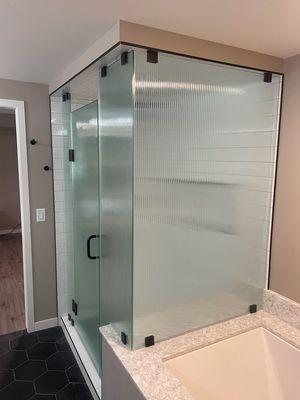 Frameless shower enclosure using 3/8" Reeded obscure glass, installed standard and glass-to-glass clamps in a sleek Matte Black finish.