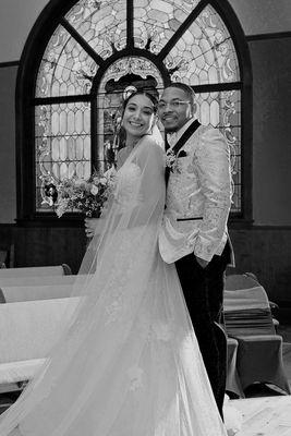 The newly married couple is photographed in front of one of three large stained glass windows.