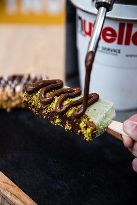 Sicilian Pistachio Paleta dipped in Dark Chocolate, topped with Pistachios, & drizzled with Nutella