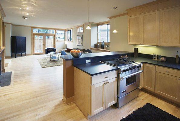 Open-concept kitchen remodel with modern black counter tops and light colored hardwood floor for an airy feel.