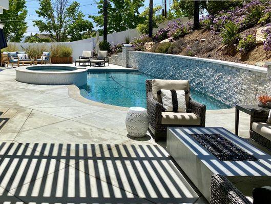 Elegant poolside retreat featuring custom pool coping and a stone retaining wall for a luxurious backyard oasis.