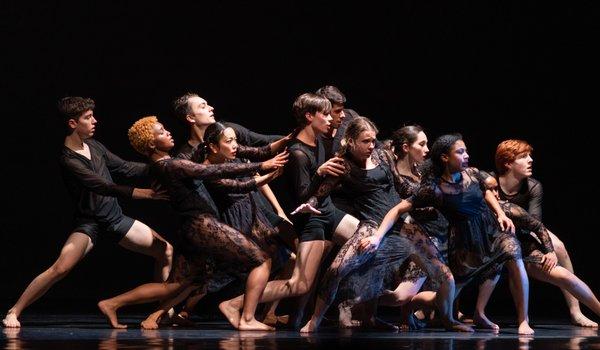 Group of dancers wearing all black shift back slightly in their stance and stare with intensity to the right