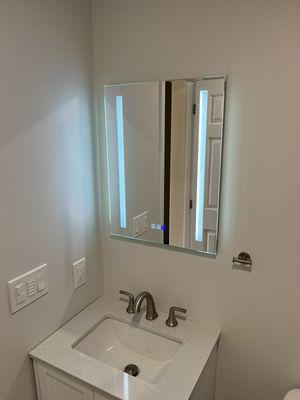 A lighted mirror on a recessed medicine cabinet over a 24-inch sink and cabinet.