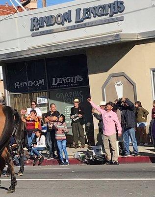 People cheering on the 38th Annual Spirit of San Pedro Holiday Parade from the sidewalk in front of Random Lengths News.