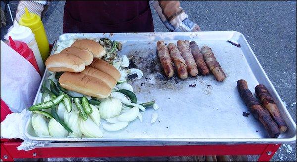 Bacon wrapped hot dogs, onion, chili peppers and buns... on a propane-fired griddle from a push cart.