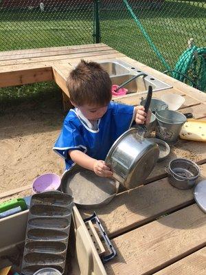 Mixing sand and water in the Mud Kitchen on the playground.