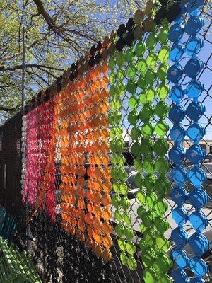 Recycled plastic can tops made into a colorful fence decoration.