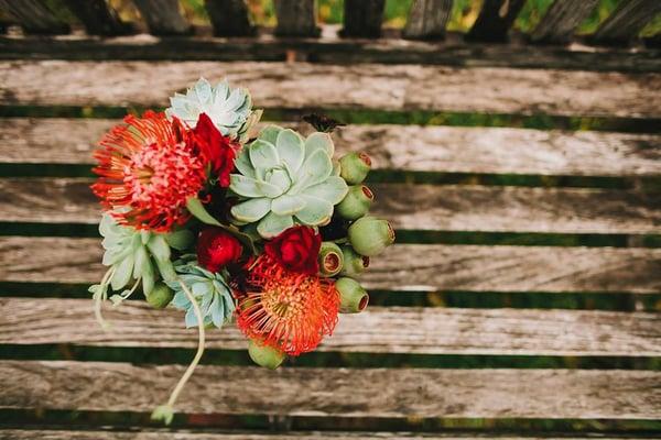 Centerpieces with pin-cushion proteas, ranunculas, sucuulents, keeping our coral red and mint green wedding colors:)