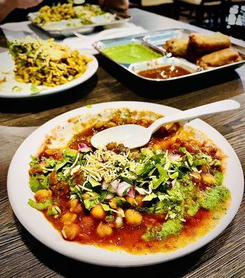 Aloo chaat in front with bhel puri in the background left, and mirchi pakora, background right. Dahi puri in the distant background.