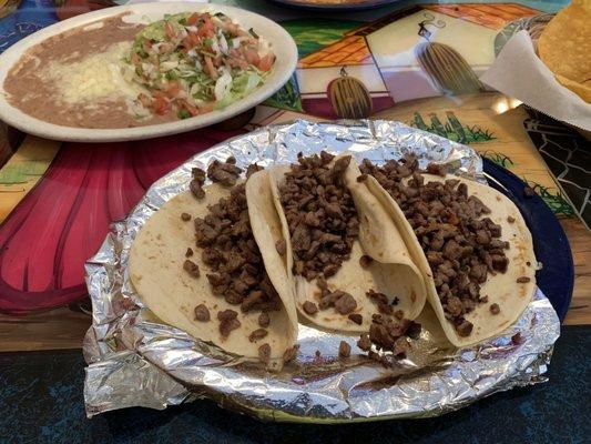 Flour tortilla asada tacos with rice and beans on the side.