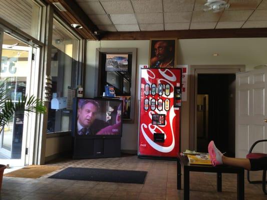 Waiting room area with TV, vending machine, Tupac picture on top, and doorway to restroom.