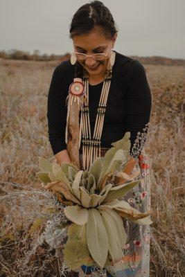 Owner and founder of Lakota Made, Megan L. Schnitker, wearing Lakota regalia and holding a bundle of mullein leaf and other medicinal plants