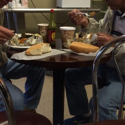 Two gentlemen enjoying a plate of chicken with a side order of fresh bread.