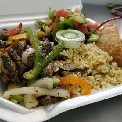 A plate full of flavor steak with pepper and onions side of rice