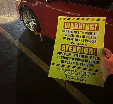 Car with boot and a flyer warning sign to pay the boot in order to remove it