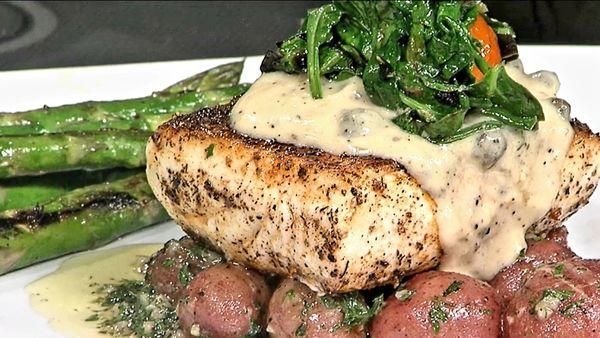 Pan seared halibut atop garlic butter baby potatoes topped with lemon caper cream sauce, sautéed spinach, and blistered cherry tomatoes