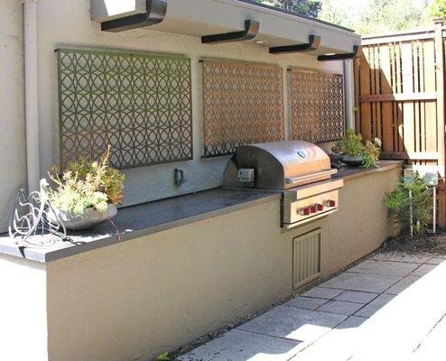 Outdoor kitchen in Rockridge is attached to a garage side. Patterned aluminium panels add dimensional interest to wall.