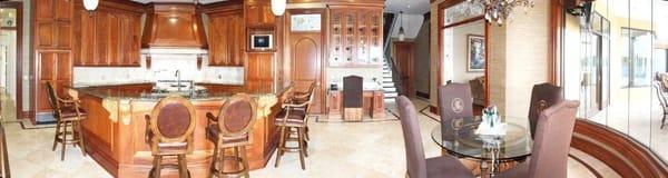 Panoramic shot of kitchen/breakfast area with curved glass walls, Sapele Mahogany Cabinetry, granite countertops, and gold gi...