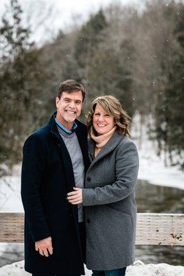 a couple smiles at the camera outdoors in winter by the Betsie River