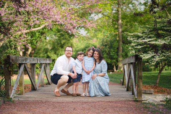 A family photo with pink spring blooms on a bridge