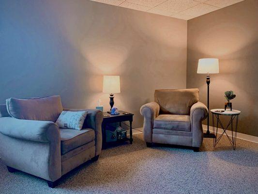 A view of my therapy office. Two tan chairs at a angle to each other with a black side table to the side.