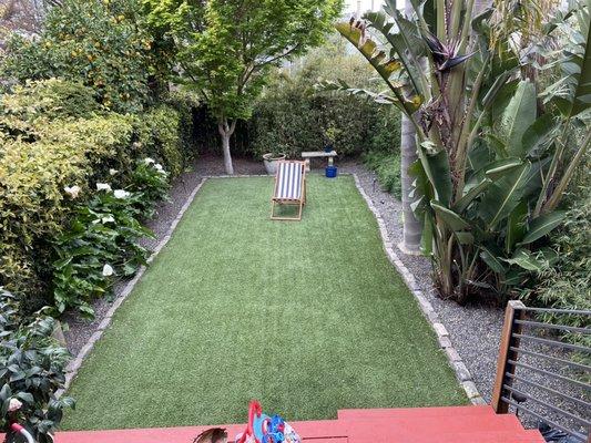 Nice backyard with artificial grass and beautiful surrounding plants.