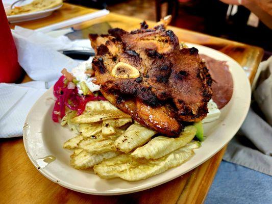 Pork chop with fried plantain, pickled veggies, refried beans, and Cole slaw.