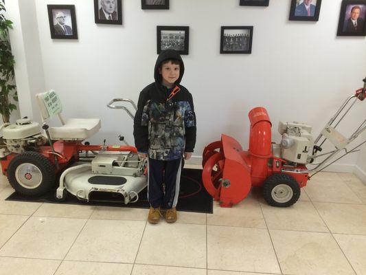 about 8 years ago our son standing near 3 antique ariens rear engine rider and ariens snow thrower at our distributor