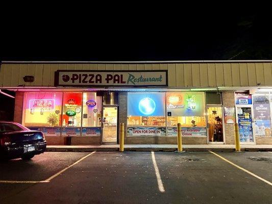 Frontage at night - pizza pick up inside on left, dining room and small bar on right